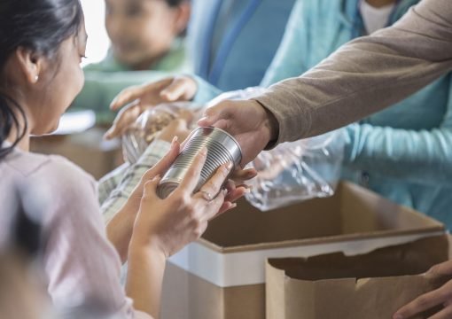 Young woman receives a canned food item from food bank. An unrecognizable volunteer hands her the canned food item.